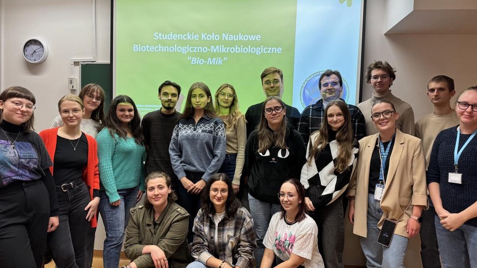 Zdjęcie uczestników zebrania inaugarcyjnego SKN Biotechnologiczno-Mikrobiologicznego. Przedstawia 18 osób na tle slajdu zatytułowanego "Studenckie Koło Naukowe Biotechnologiczno-Mikrobiologiczne "Bio-Mik"".